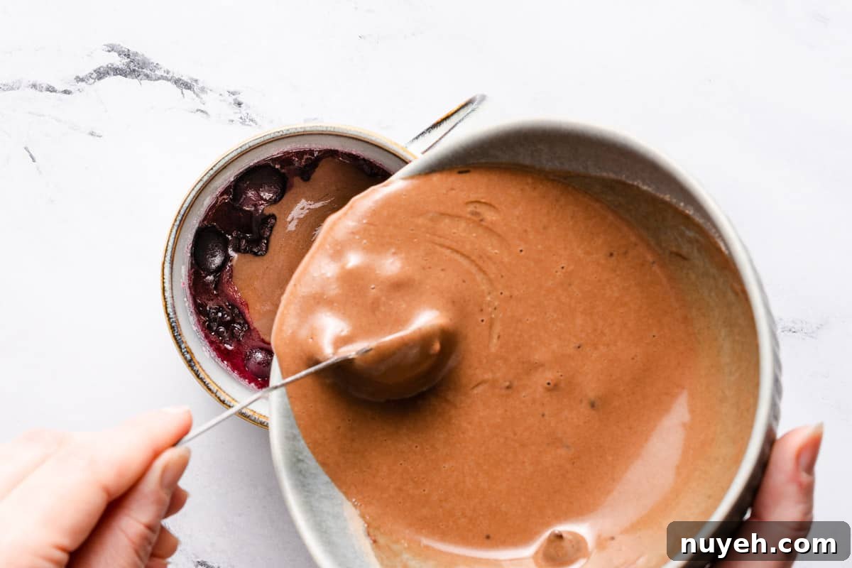 cake batter being poured on top of berries in mug