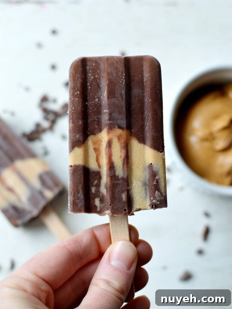 close up of a banana popsicle with chocolate and a peanut butter layer