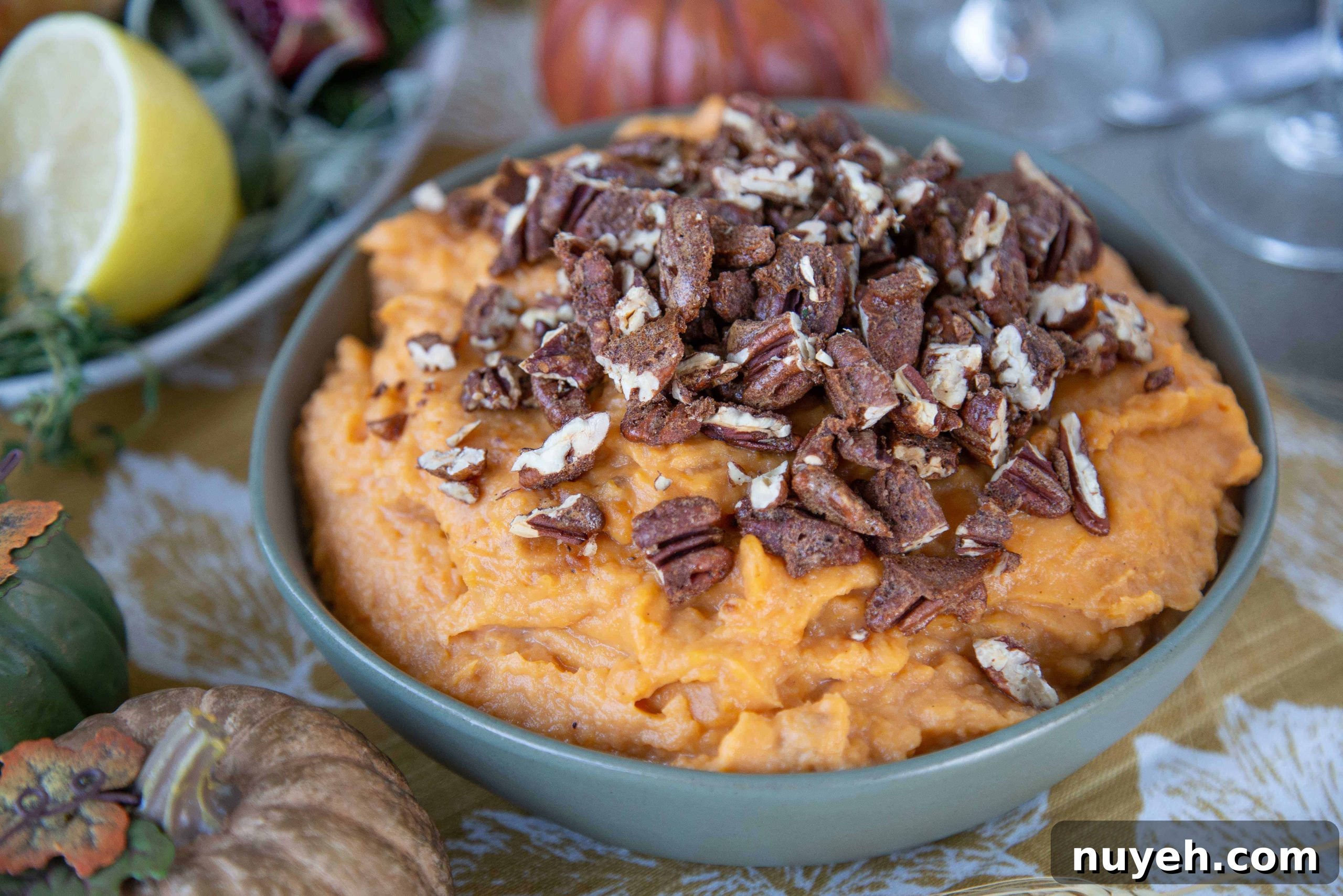 Mashed Sweet Potatoes with Spiced Pecans in a green bowl on a table with gold, green, and orange faux pumpkins.