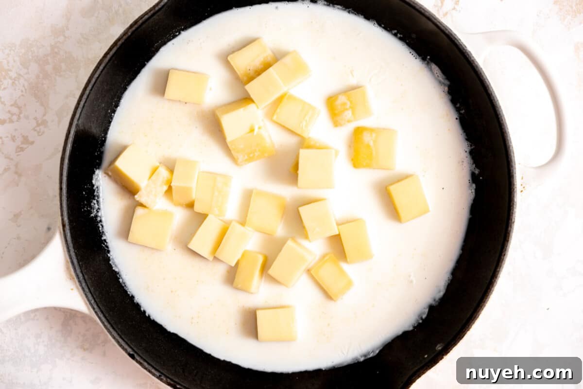 Skillet with cream and chunks of white American cheese melting. 
