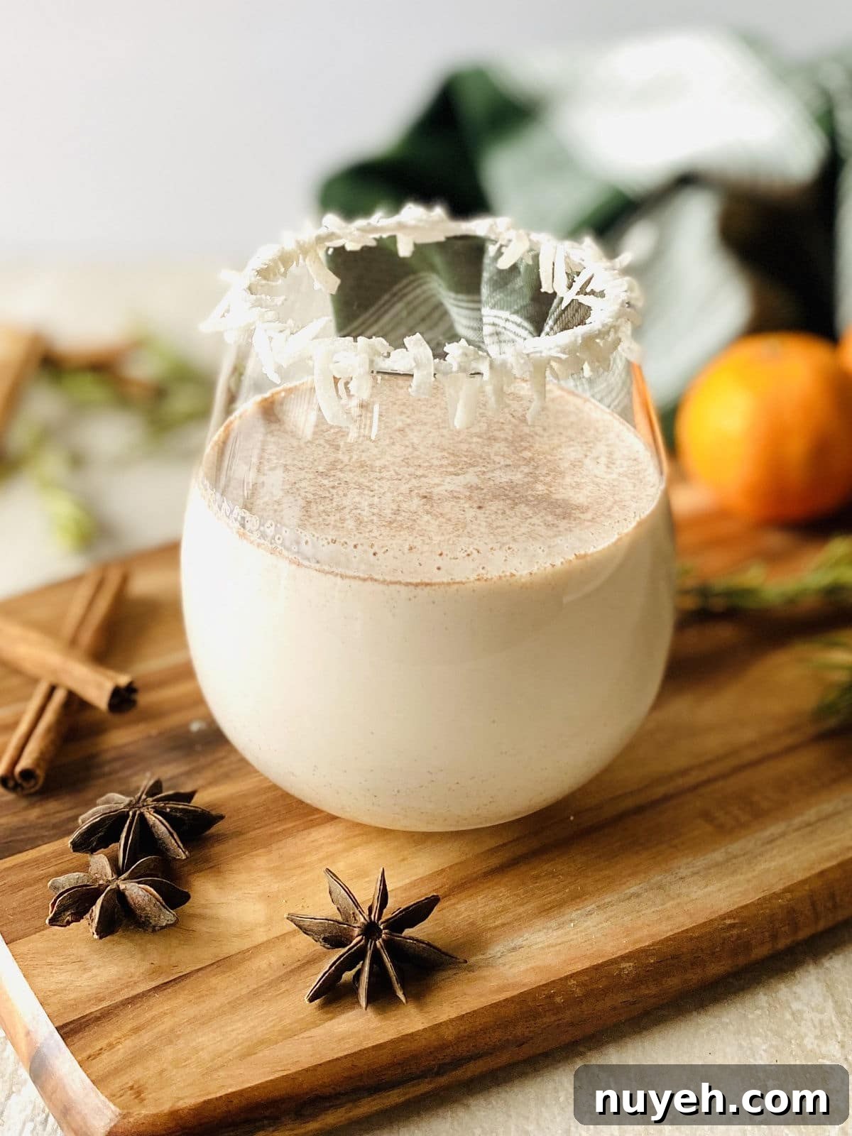 Bacardi Coquito Recipe: Creamy Puerto Rican Coconut Rum 2 a glass of coquito with a coconut rim on a wood cutting board surrounded by spices, oranges and rosemary