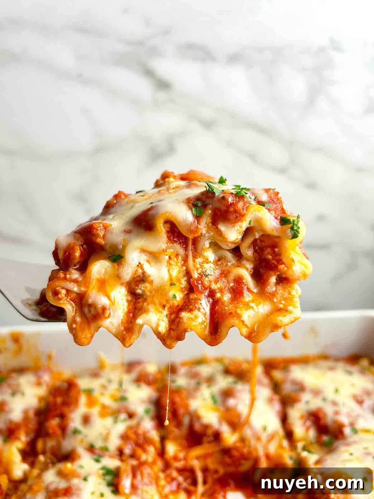 spatula lifting up lasagna roll up; sauce and cheese oozing out.