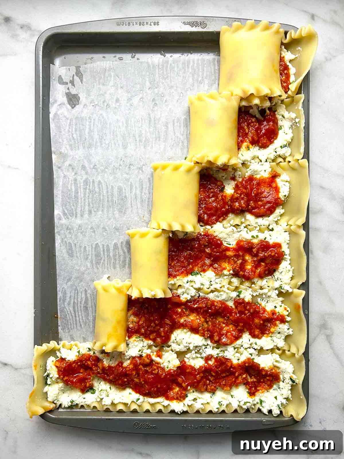 lasagna rolls being rolled on baking sheet.