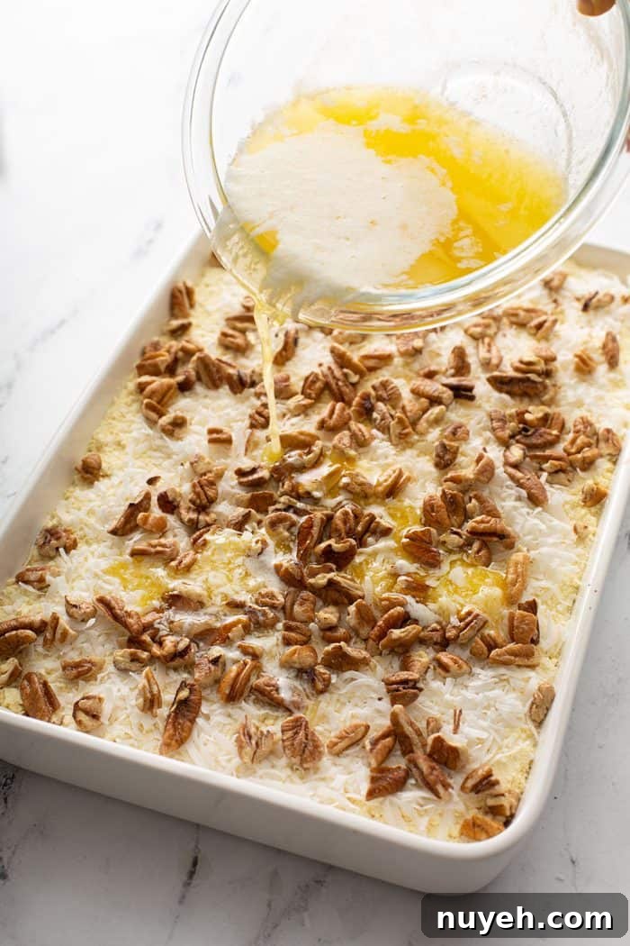Melted butter being drizzled over cake mix, coconut, and pecans in a cake pan