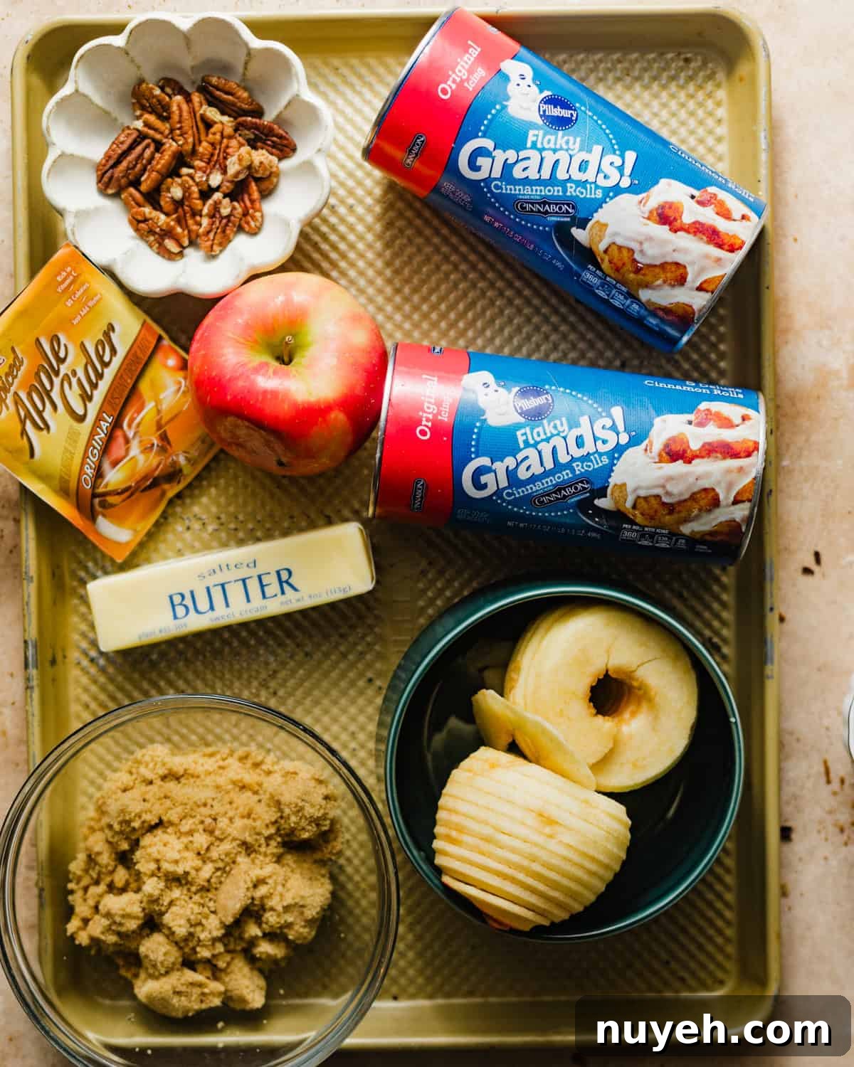 ingredients to make apple monkey bread - apples, pecans, apple cider packets, pillsbury grands cinnamon rolls, butter, lemon juice, brown sugar, and cinnamon.
