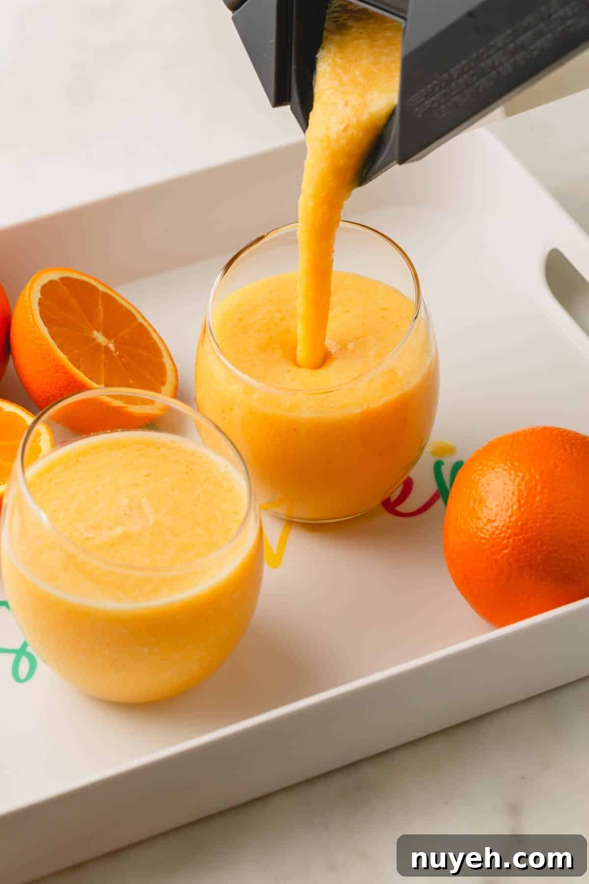 A coconut orange Julius drink being poured into two glasses from a blender.