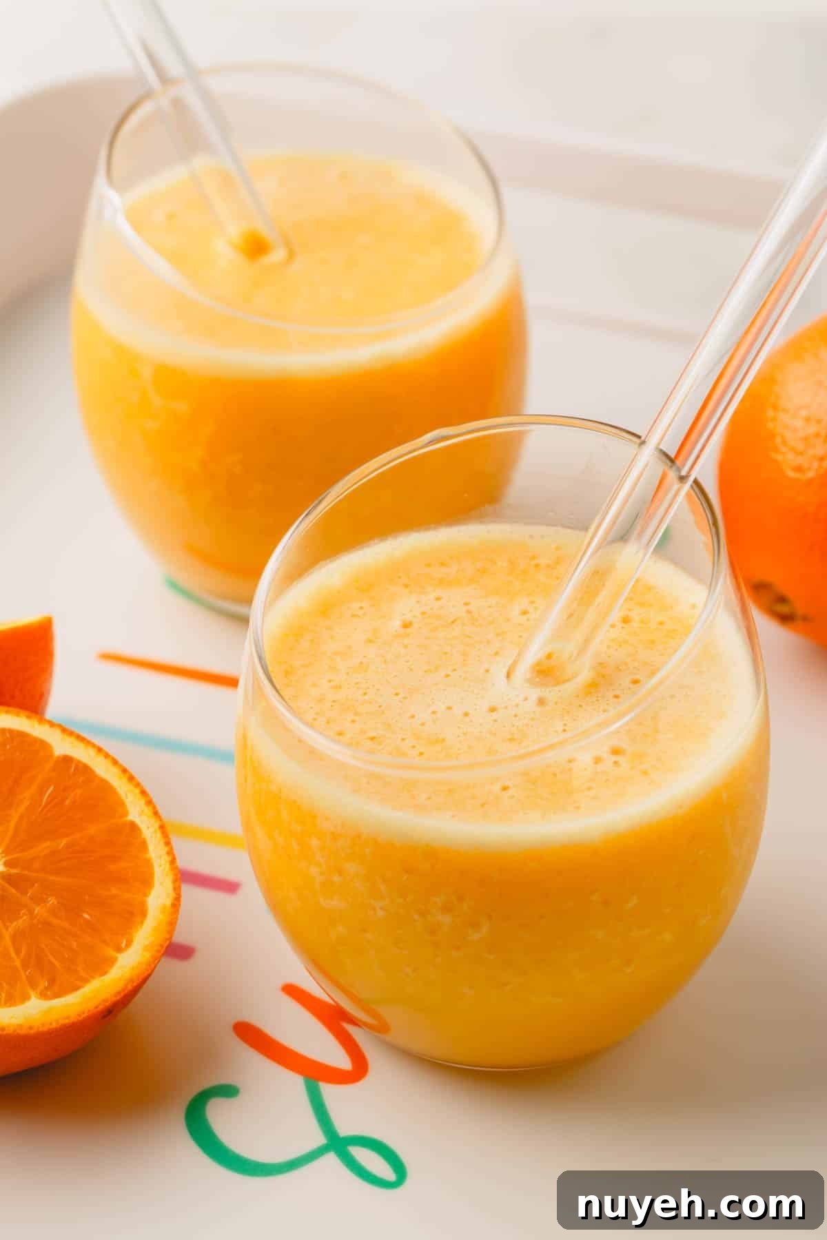 Two glasses of a coconut orange Julius drink with glass straws.