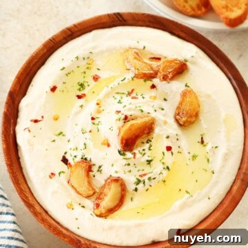 Feta dip with roasted garlic cloves in a wooden bowl on a cream board.
