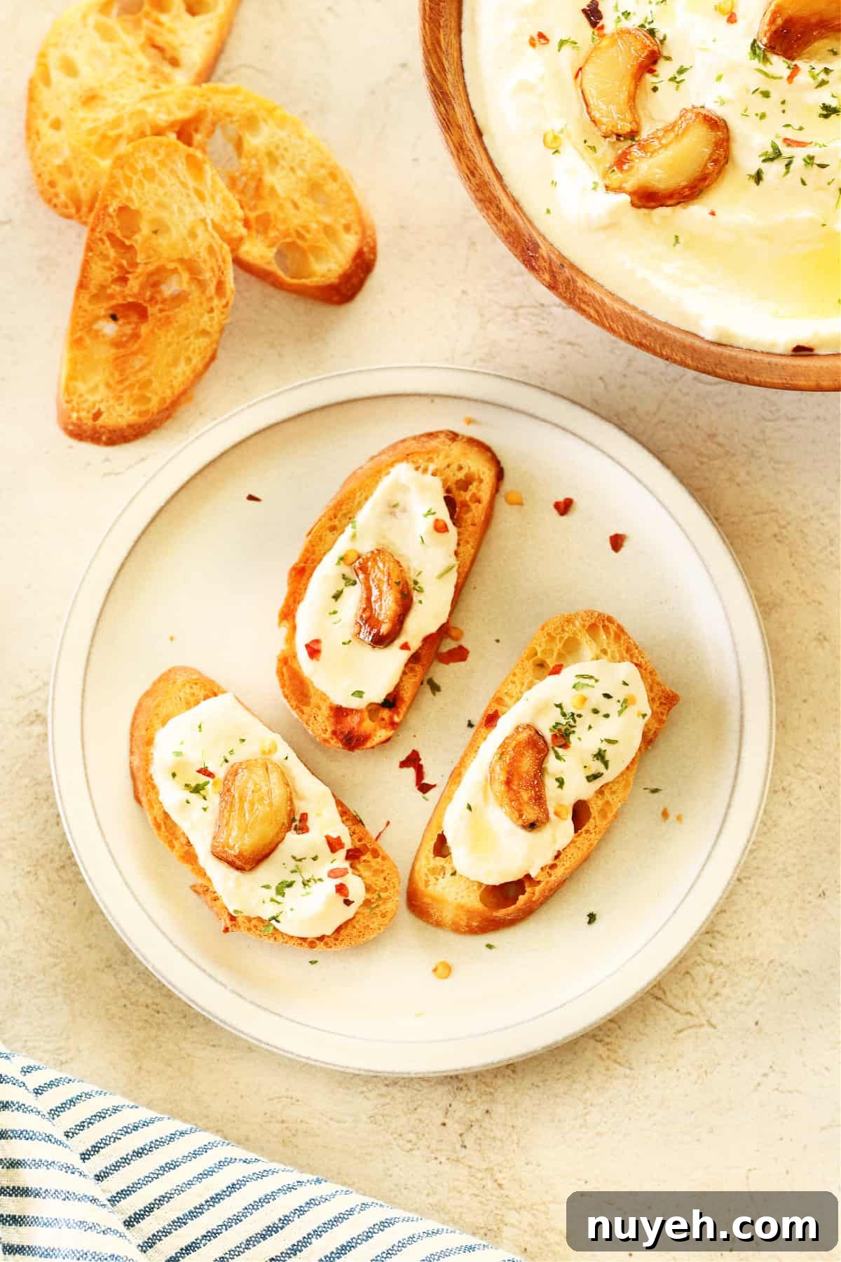 Three slices of baguette with feta dip and roasted garlic on a small plate.
