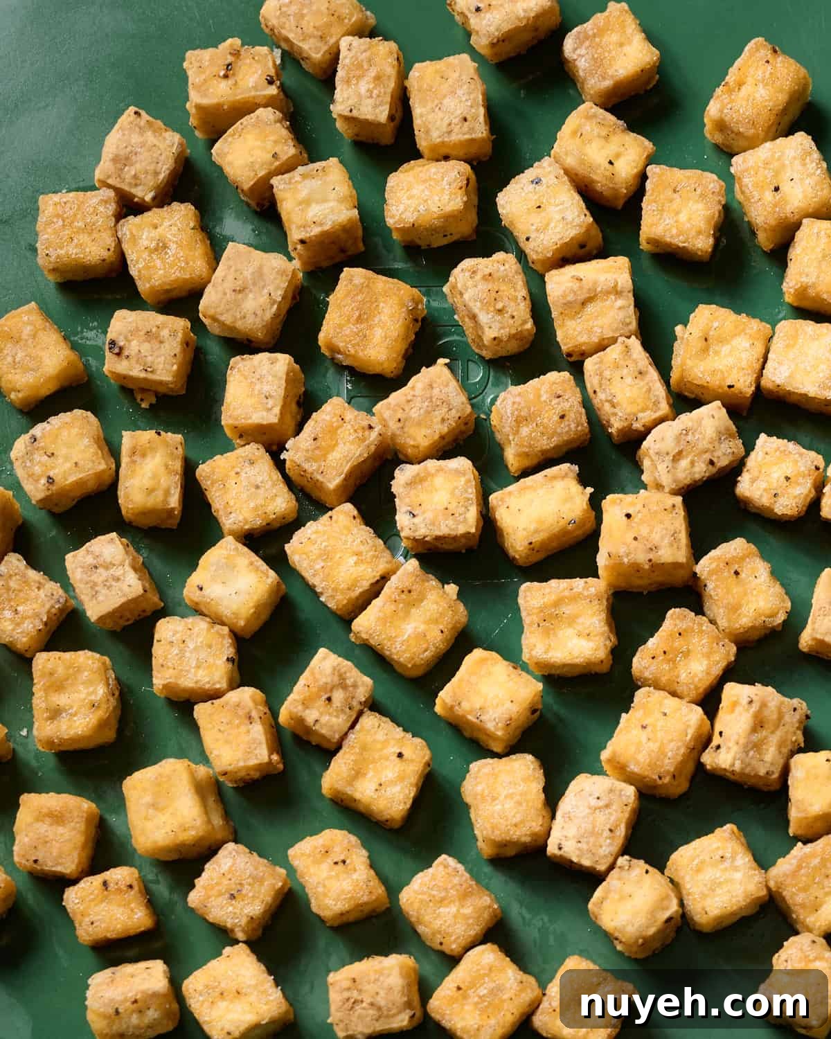 crispy baked tofu cubes on a green sheet pan. 