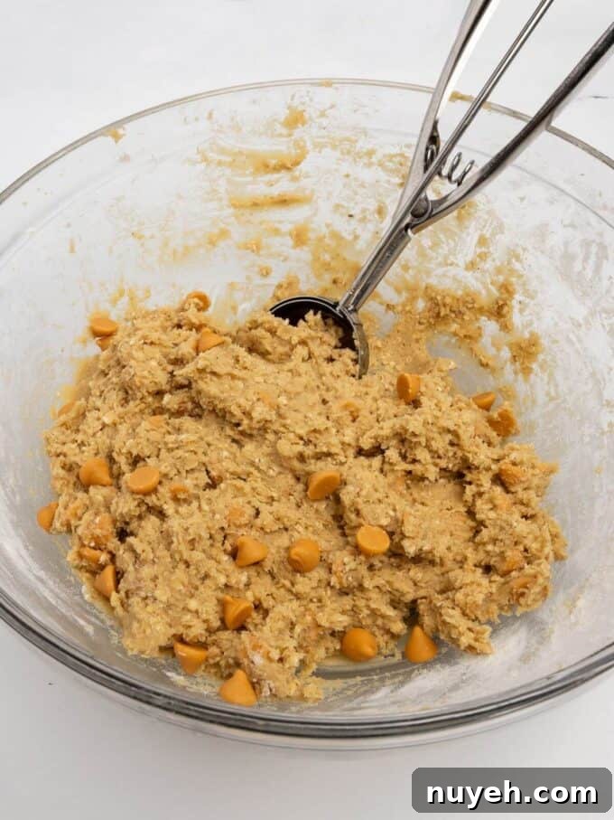 oatmeal scotchie cookie dough in glass mixing bowl with cookie scoop