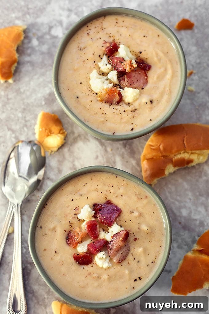 Two grey bowls of Cauliflower Bacon Chowder surrounded by torn bread and two silver spoons