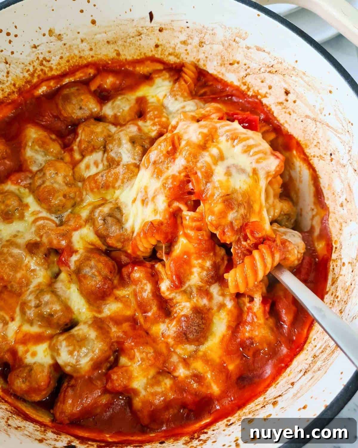 Close up of a freshly baked sausage pasta topped with melted strechy cheese