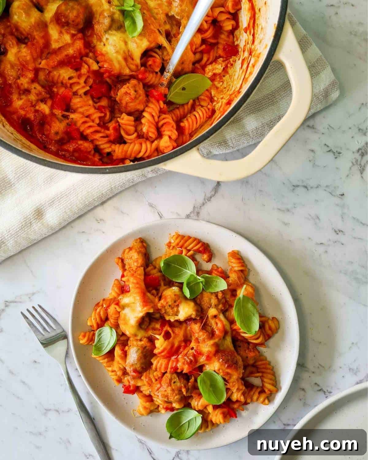 A small plate of sausage pasta and a pot full of baked pasta in the top left hand corner