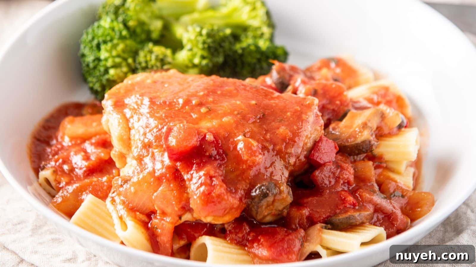 A white plate with pasta with chicken and sauce on it along with broccoli