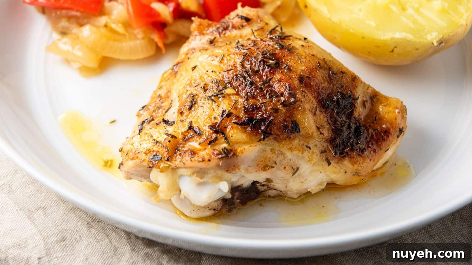 A white plate with a chicken thigh on it with vegetables and potato