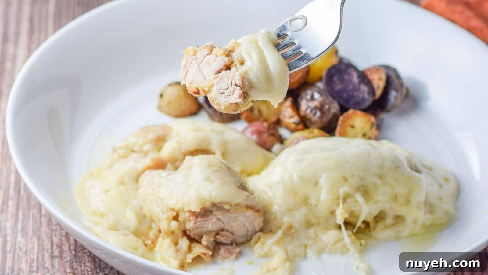a fork with some chicken and swiss cheese on it over the plate with the chicken and potatoes