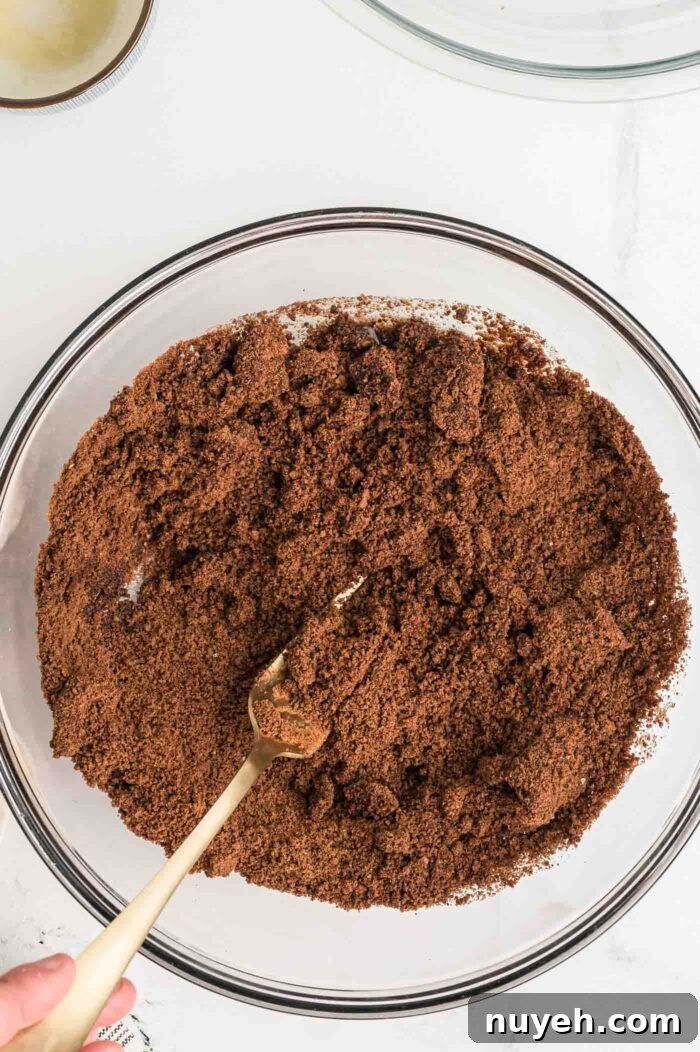 Mixing crushed chocolate graham crackers and melted butter together in a bowl with a fork.