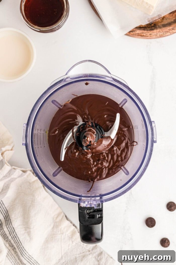 Melted chocolate in a food processor container with a few chocolate chips sprinkled around beside the container.