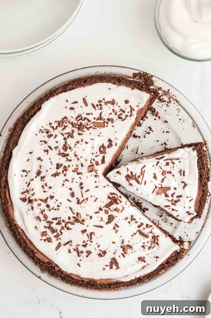 Overhead view of a chocolate pie topped with whipped cream and chocolate shavings. Once slice of pie has been removed from the pie and another slice is ready to be served.