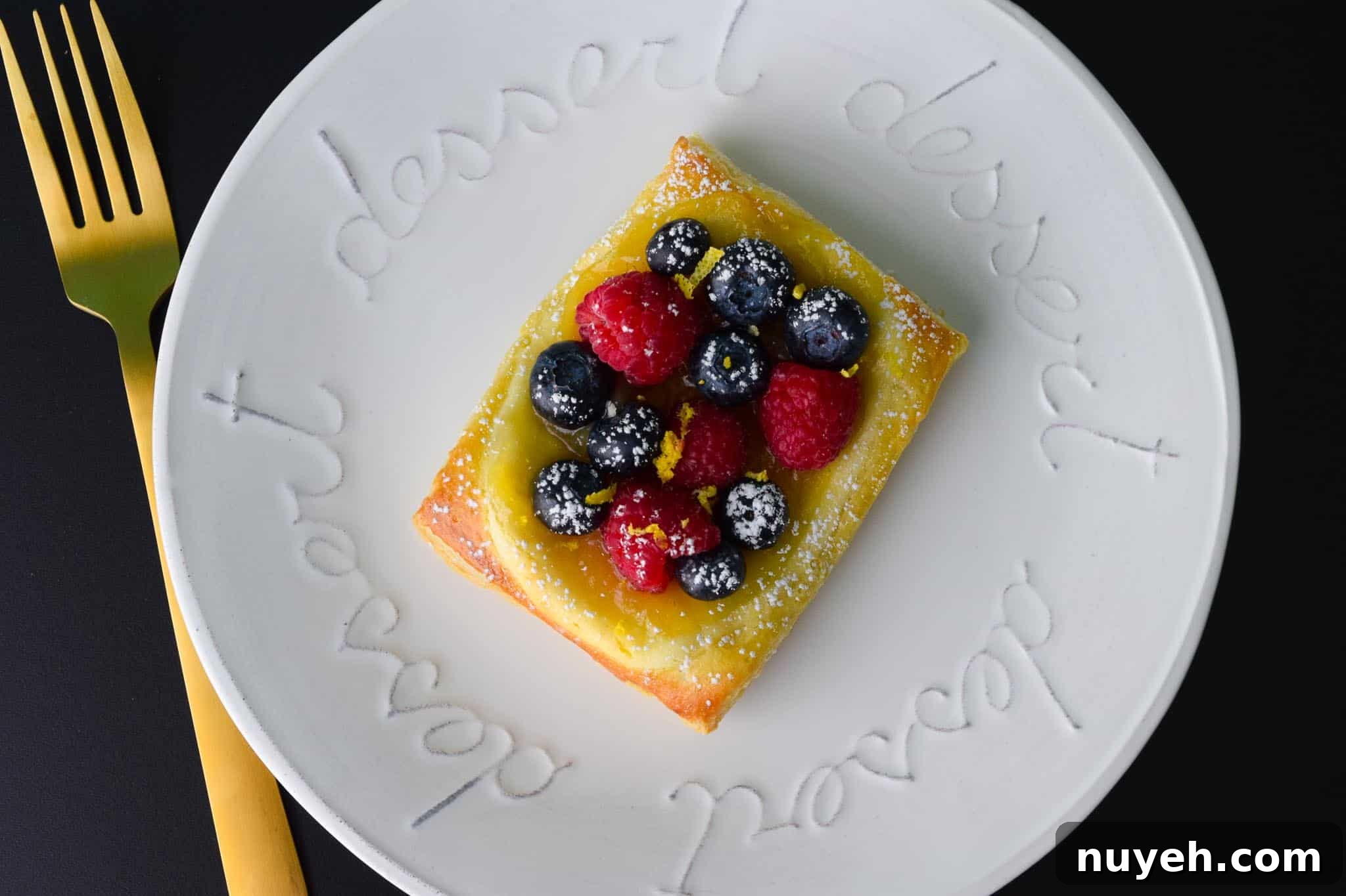 Lemon and Berry Cheesecake Puff on white dessert plate with gold fork overhead shot