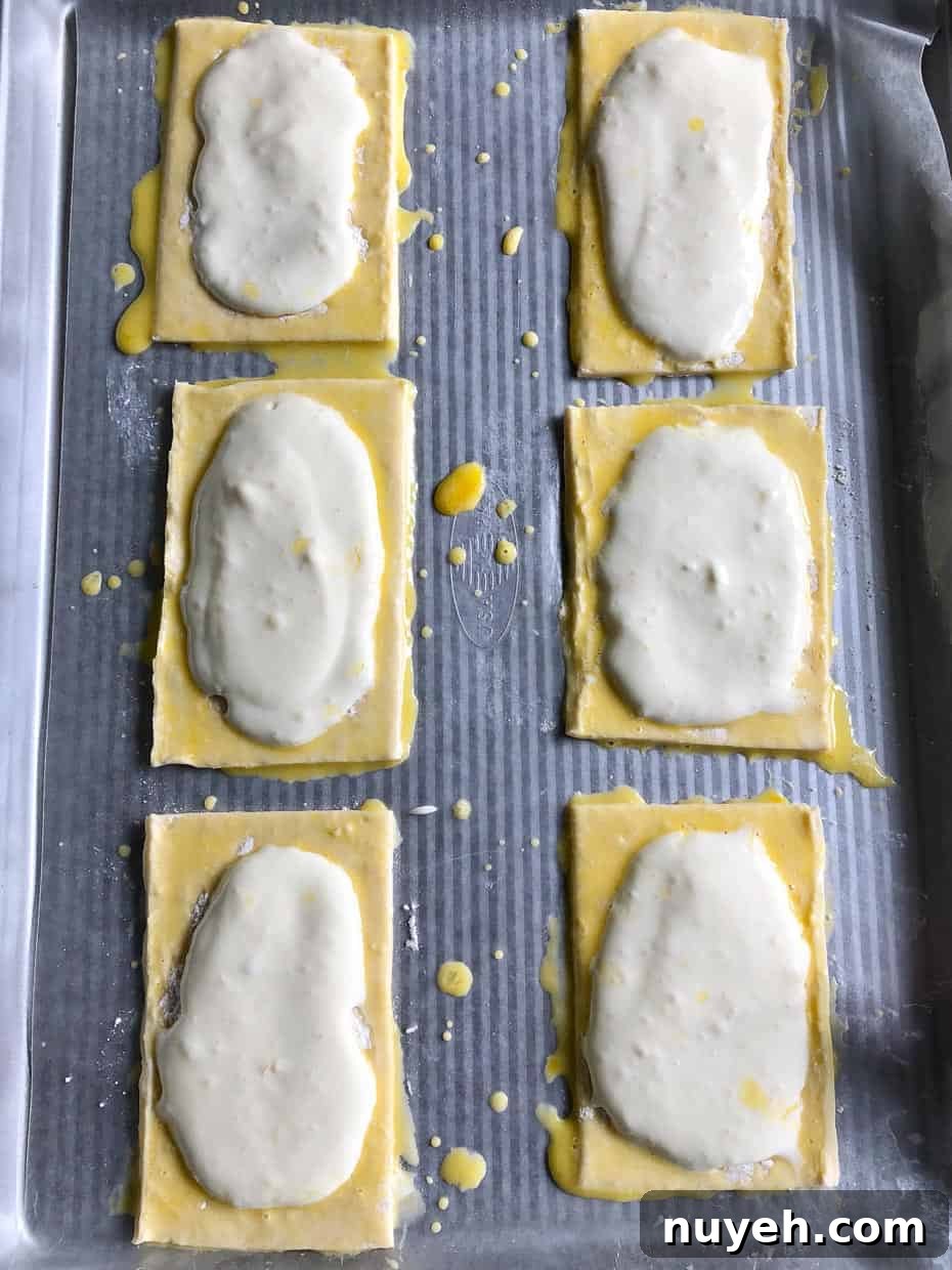 Lemon and berry cheesecake puffs on baking sheet topped with cheesecake mixture and egg wash