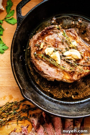 A bone in seared ribeye in a skillet with garlic and butter melted in the drippings