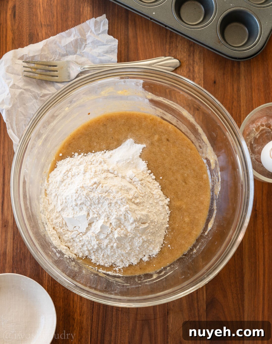 flour sitting on top of wet banana bread mixture in bowl.