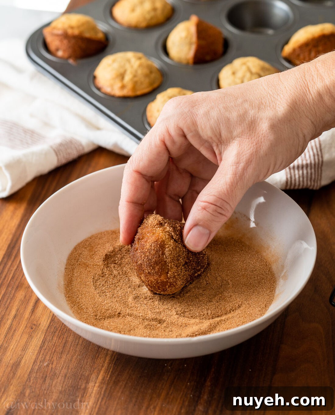 rolling muffins in cinnamon and sugar mixture in white bowl.