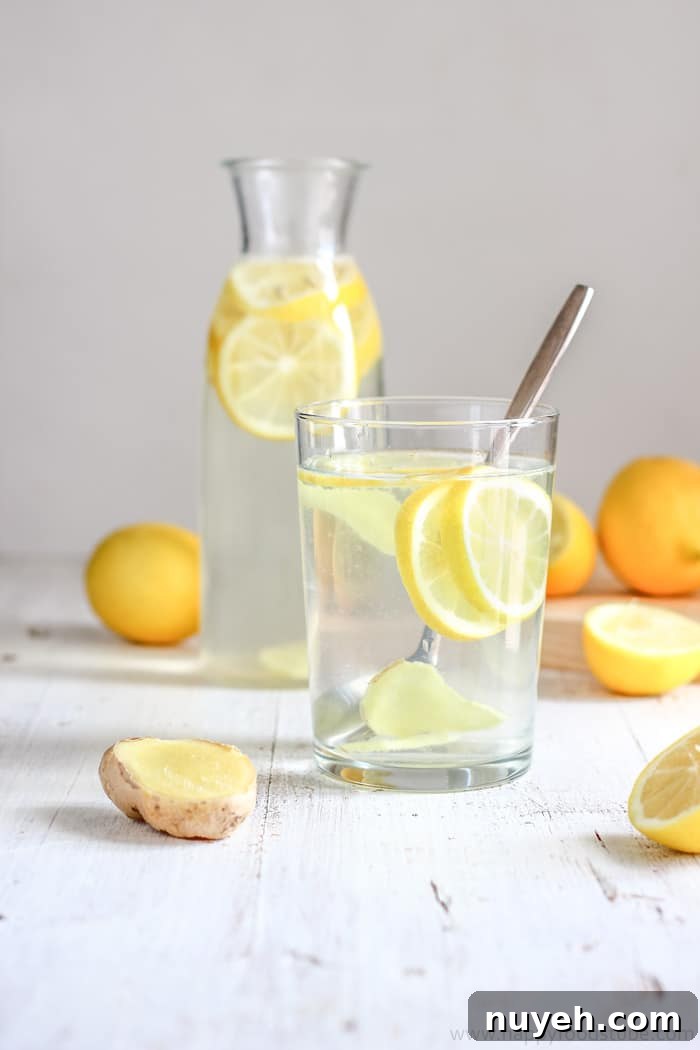 Refreshing homemade drink with lemon and ginger served in a glass, with whole lemons in the background.