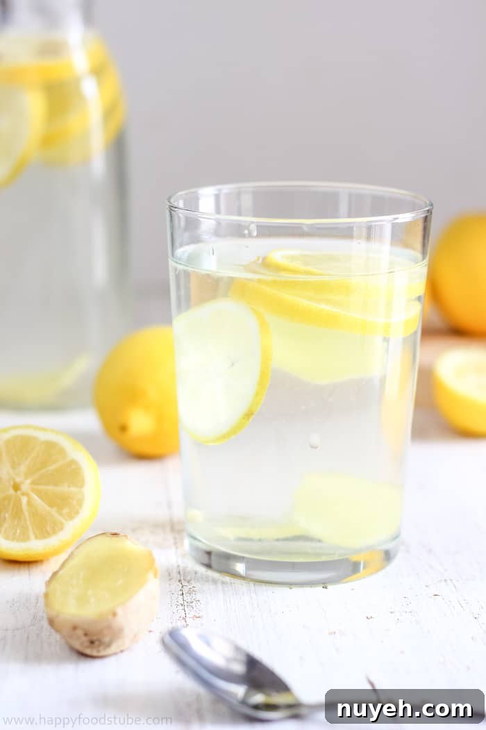 Glass filled with sliced lemon and ginger in water, surrounded by fresh ingredients.