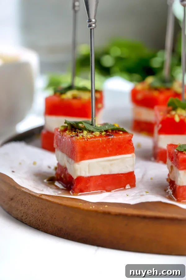 Close-up of a watermelon feta bite on a skewer with hot honey balsamic glaze, a fresh mint leaf, and crushed pistachios.
