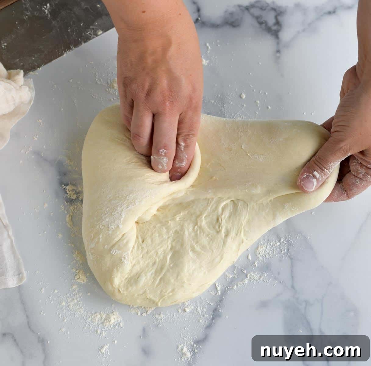 Two hands shaping a loaf of sourdough on a countertop.