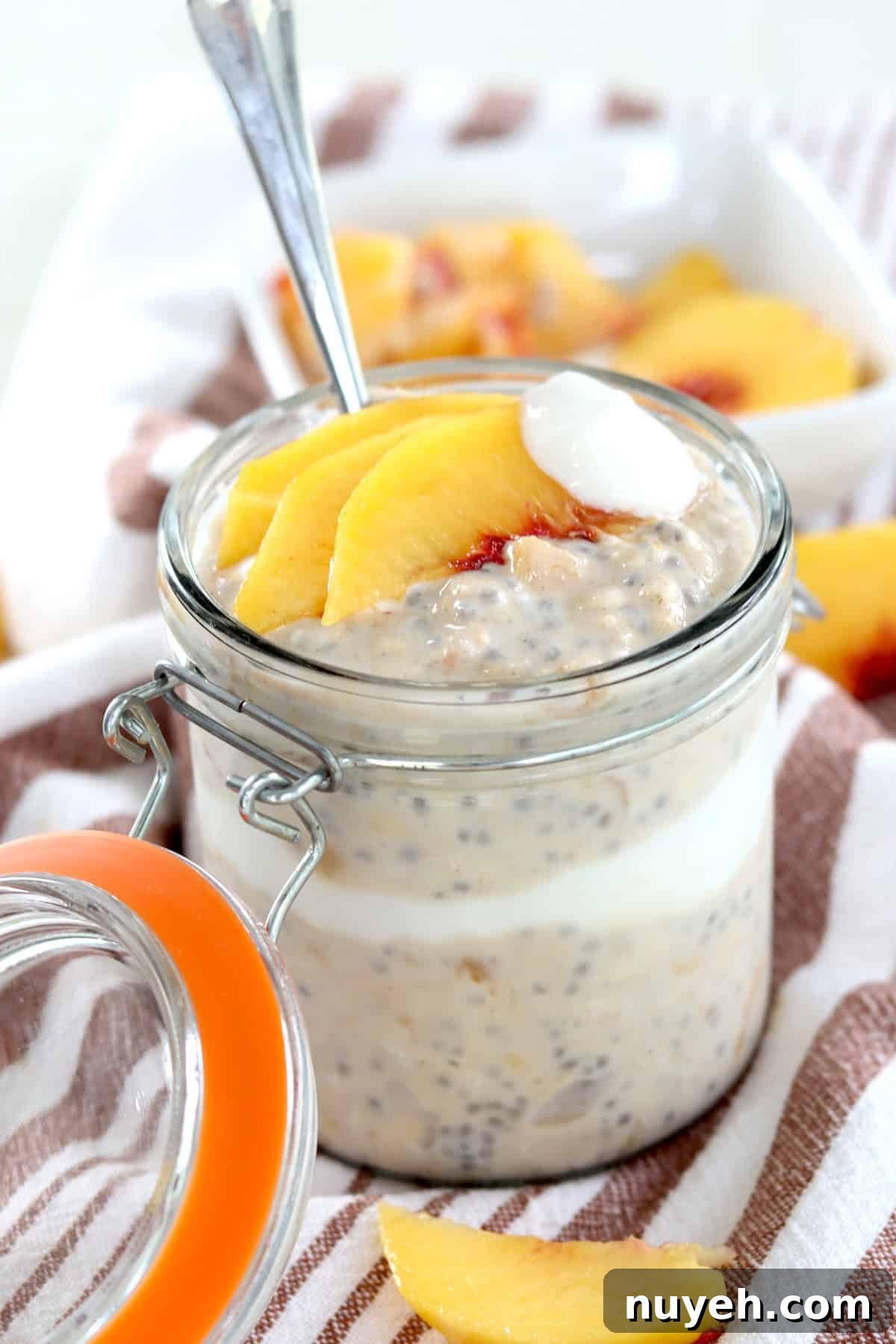 A clear lidded jar layered with overnight peach oatmeal yogurt and peaches.