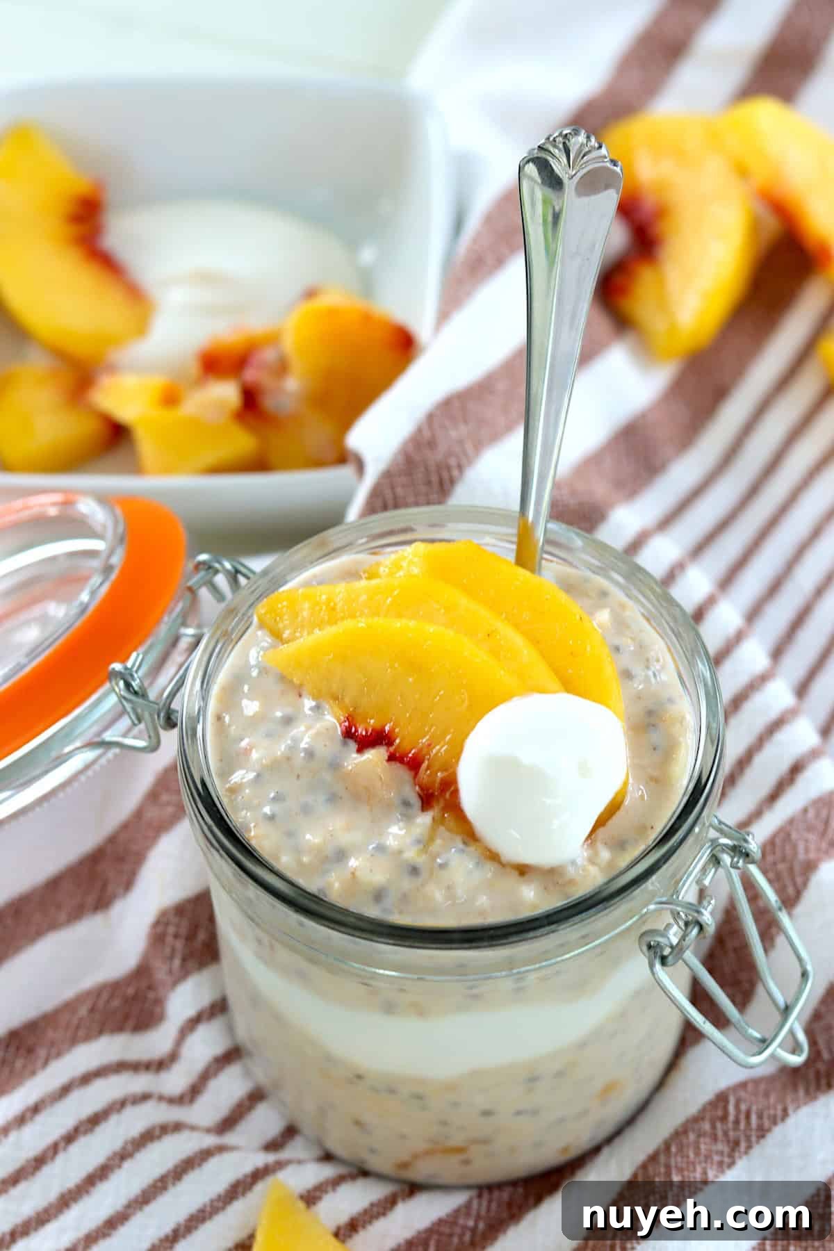 A jar of overnight peach oatmeal with thinly sliced fresh peaches and a dollop of yogurt.