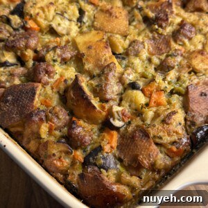 Sausage and Leek Bread-Pudding-Style Stuffing 5 A close-up of a baked casserole dish filled with bread stuffing, featuring browned bread cubes, sausage, carrots, celery, and herbs. The top is golden and crispy.