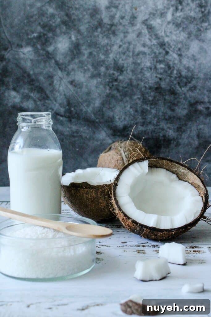 A fresh coconut cut in half next to a glass bottle coconut milk. 