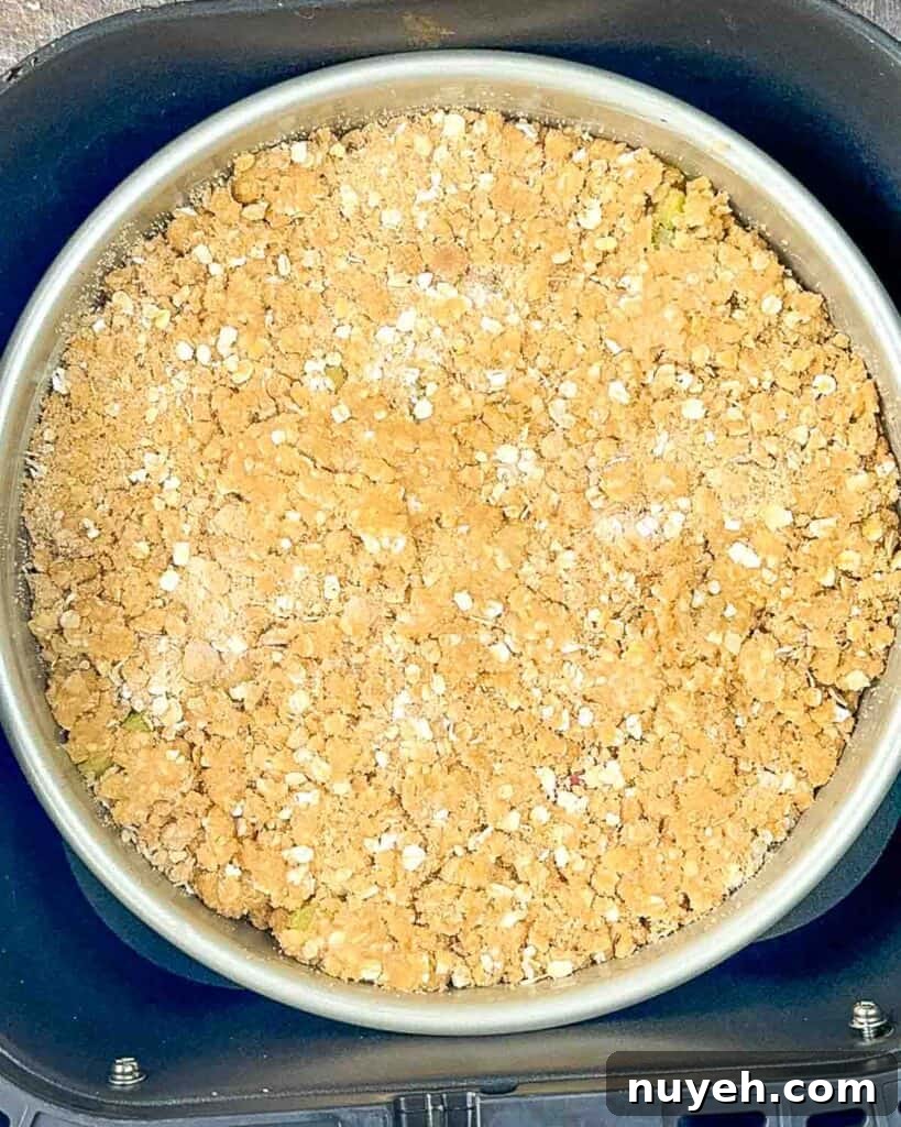 A cake pan filled with the prepared rhubarb crisp in the air fryer basket, ready to cook.