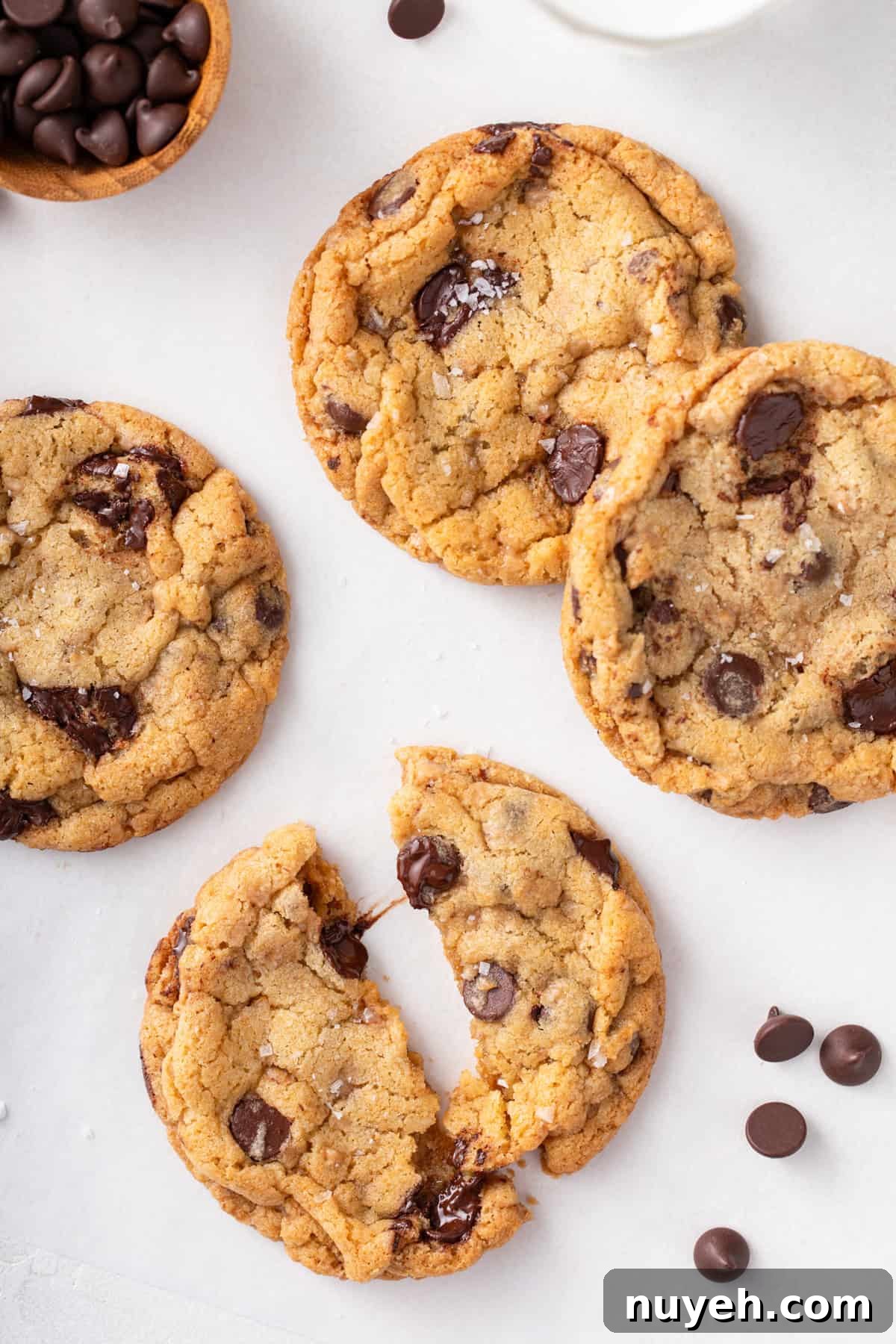 Several heath bar cookies on a countertop. One cookie is cut in half to show the gooey chocolate chips.