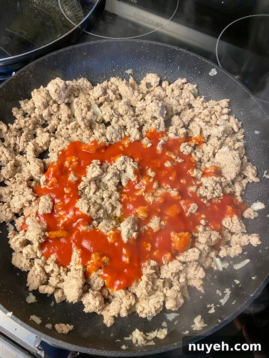 Tomato sauce poured over cooked ground turkey in a skillet