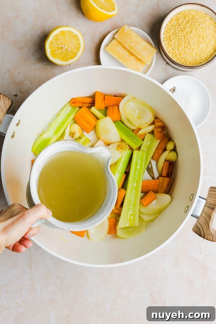 Chicken broth being added to vegetables in a large, white pot