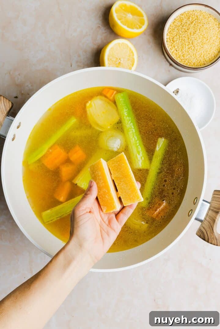 Parmesan rinds being added to vegetables in a large, white pot