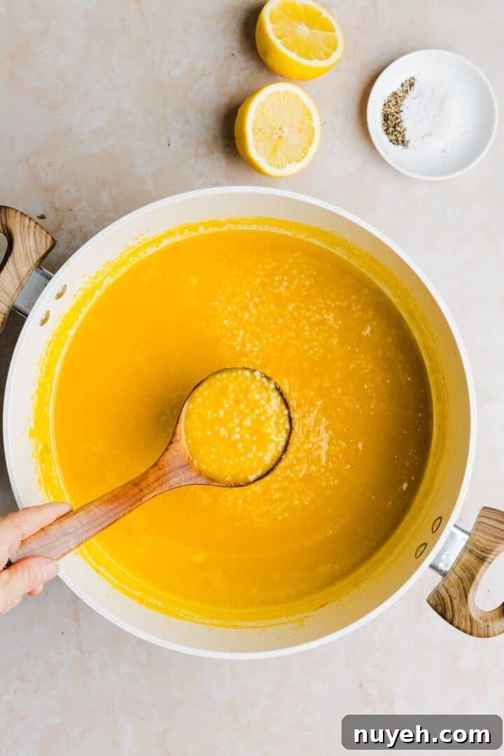 Ladle showing pastina soup in a large white pot