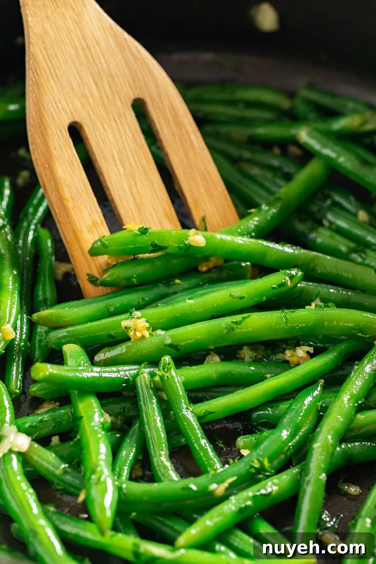 A close up image of green beans in a pan with a wooden spatula in it.