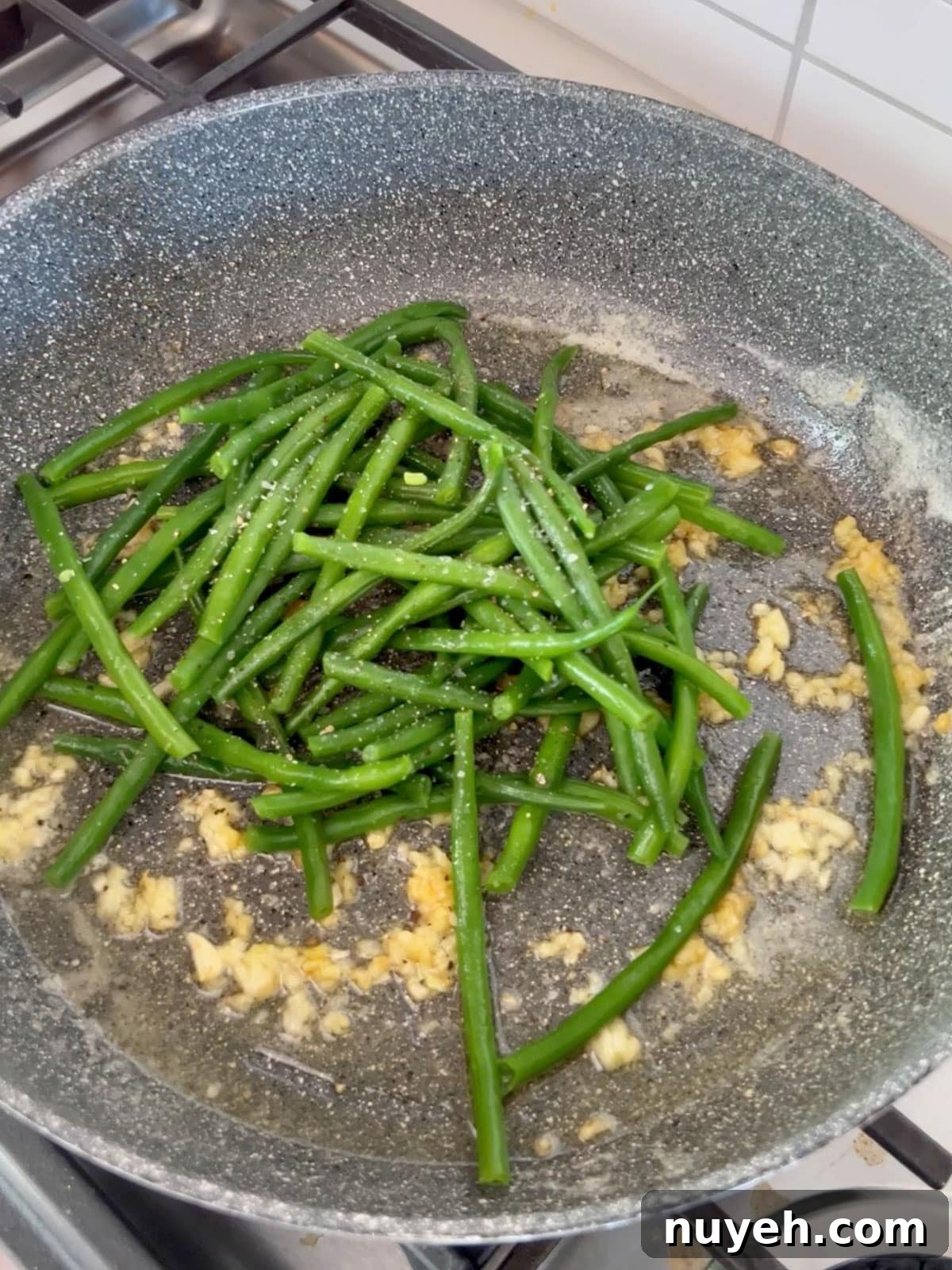Green beans added to the sauté pan with garlic.