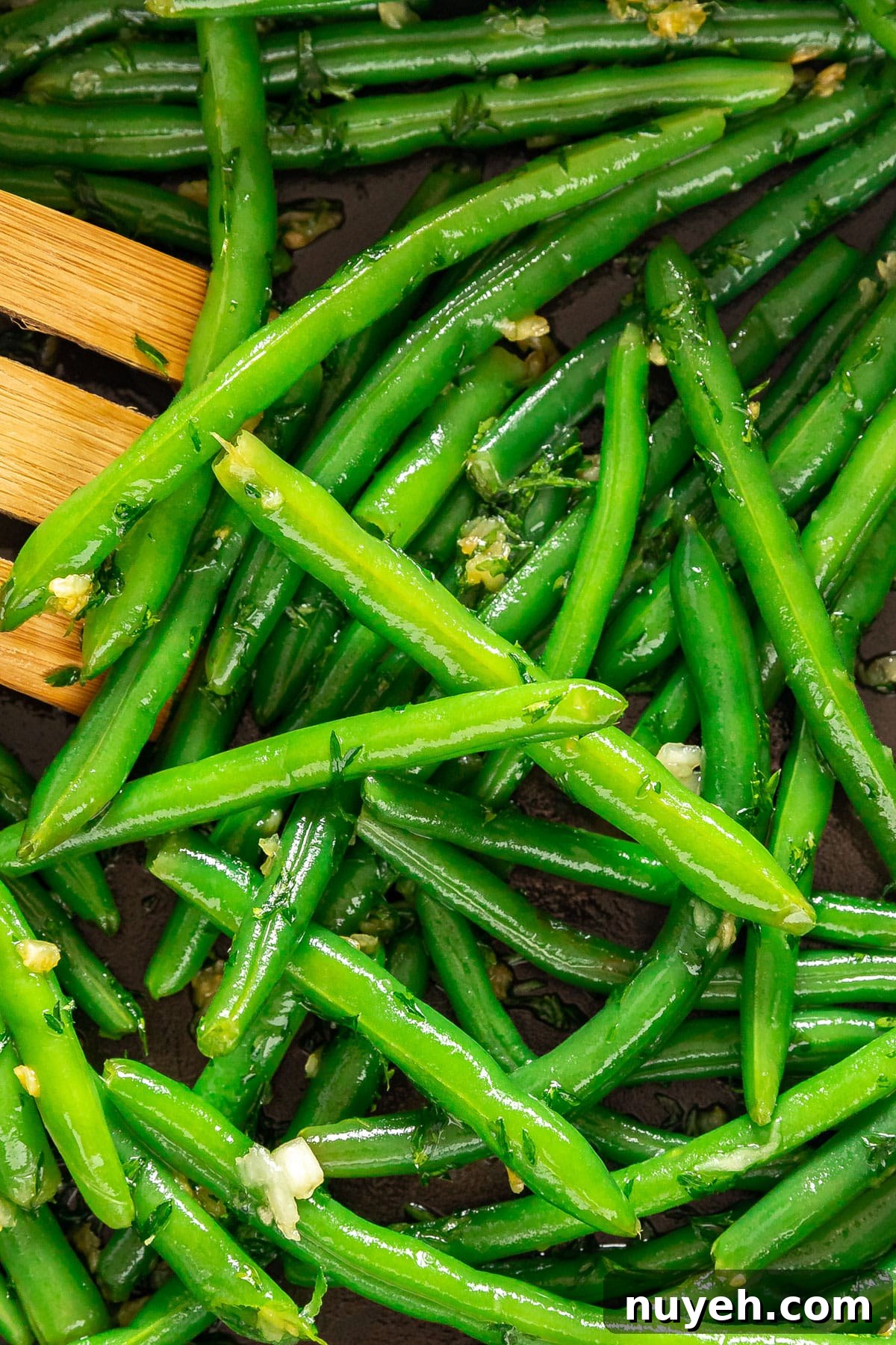 A close up image of green beans in a pan with a wooden spatula on the side.