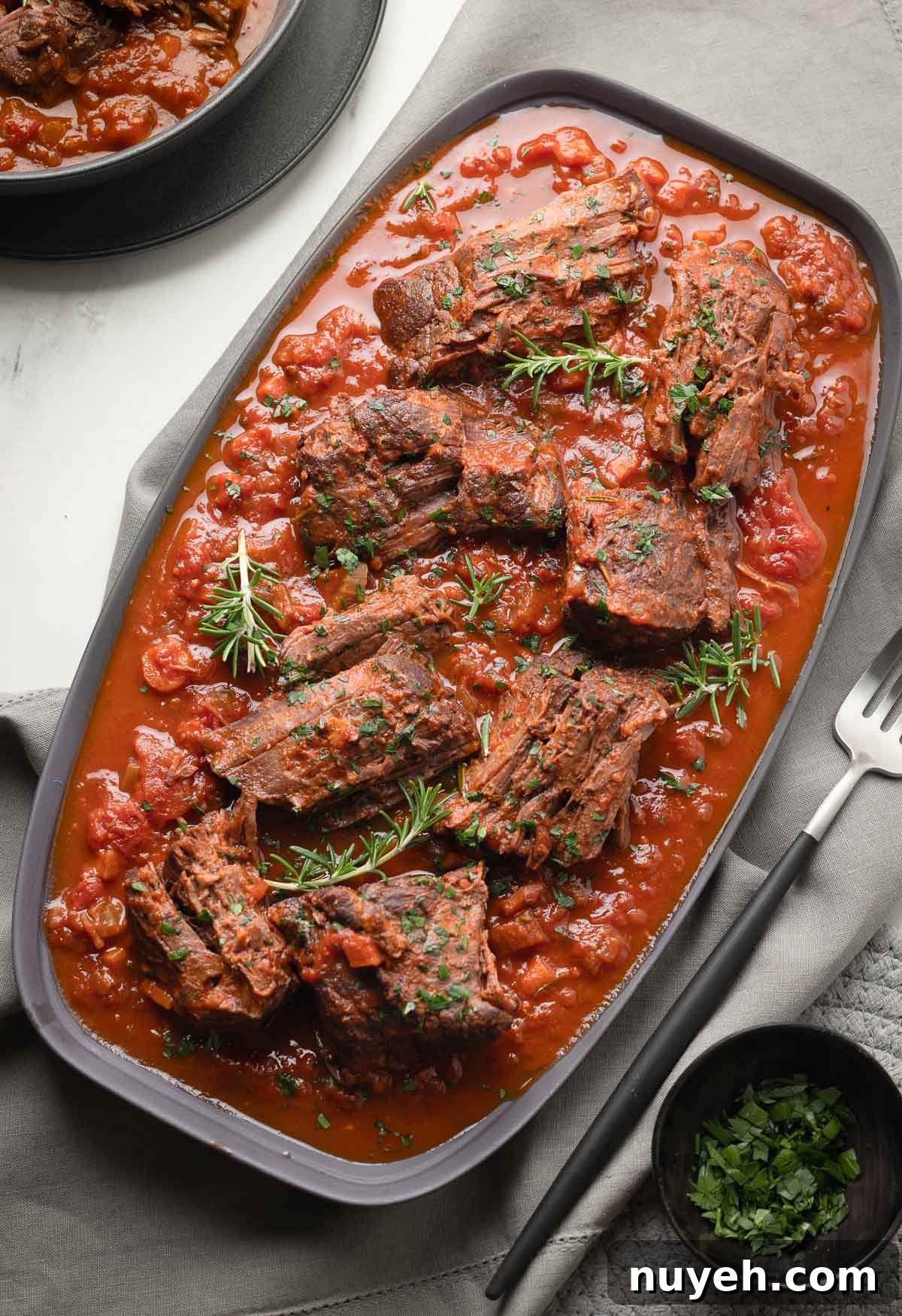 Italian pot roast, called stracotto, with chunks of meat and red sauce on a gray platter.