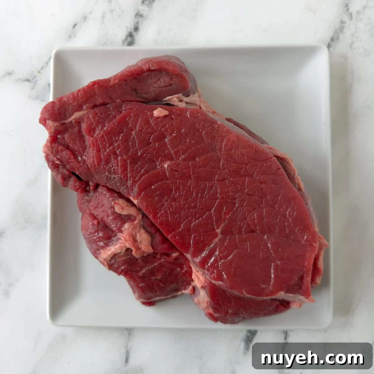 a raw red chuck roast on a plate on the counter.