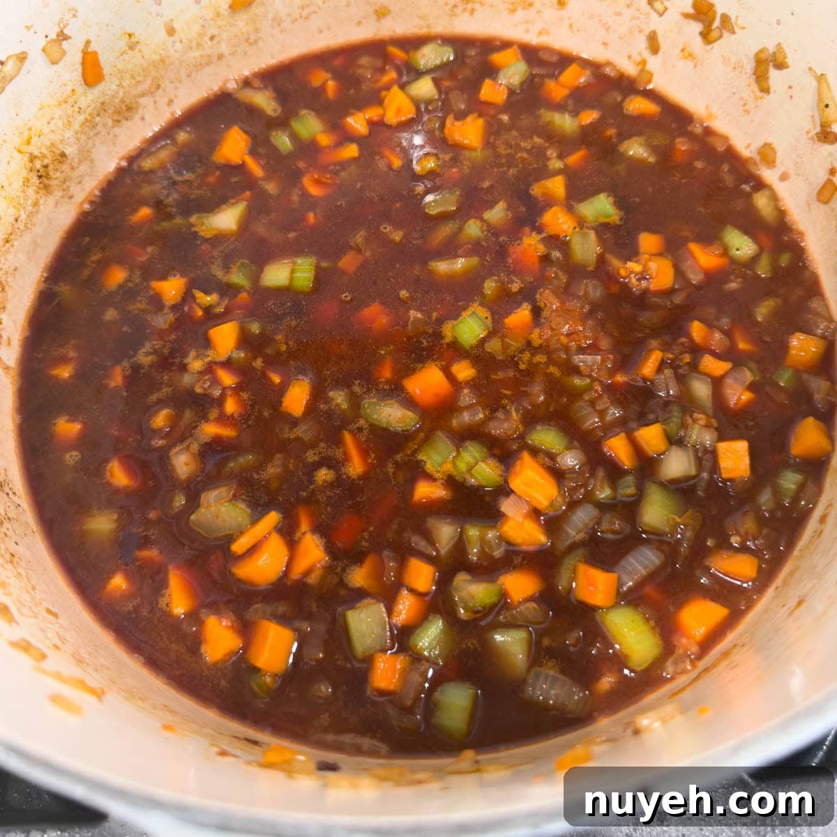 Red wine reducing in a large pot with vegetables to create a braising base.