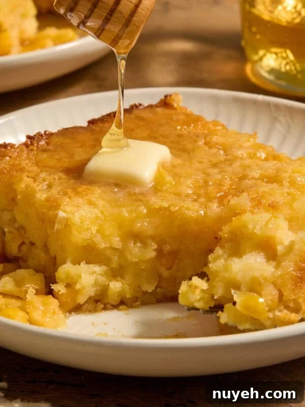 Sweet jiffy cornbread casserole on plate with honey drizzling over top.
